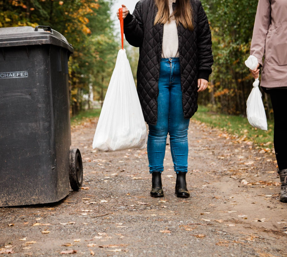 Deux jeunes femmes tenant des sacs à déchets à côté d'un bac à déchets