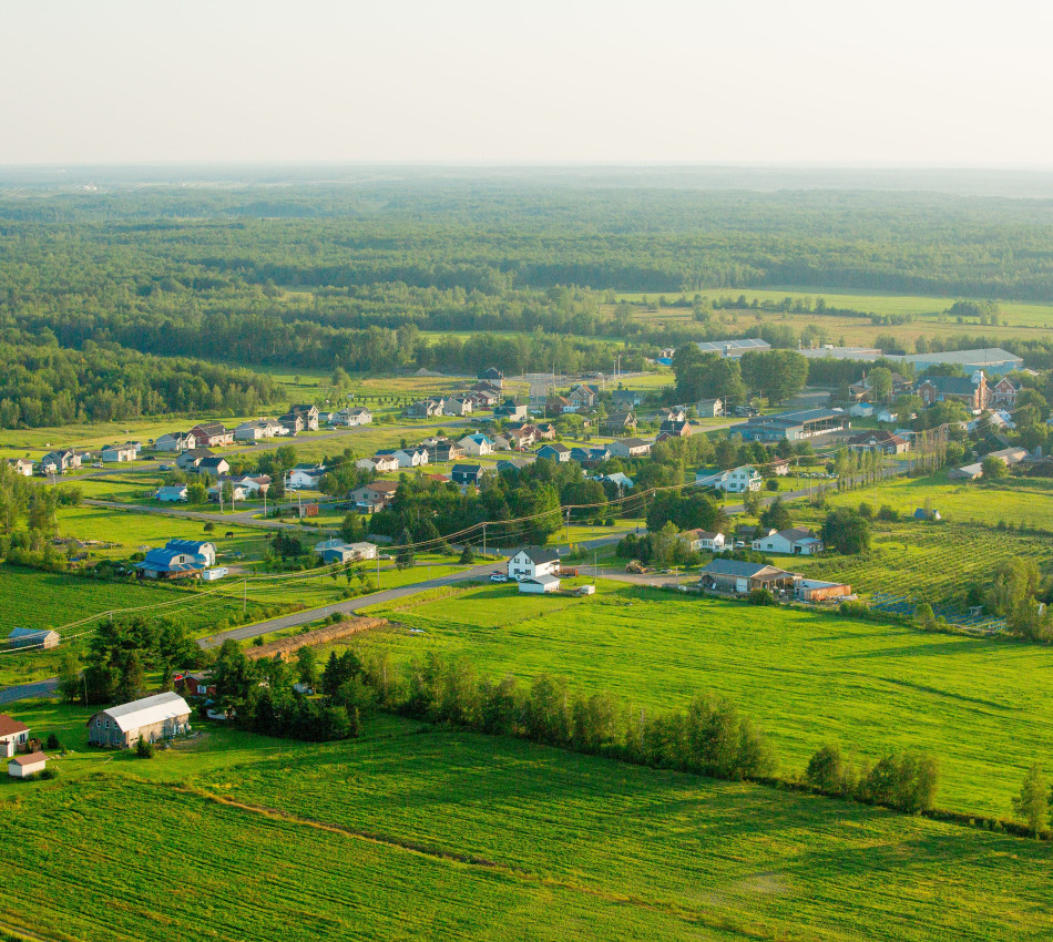 Vue aérienne de la Municipalité de la paroisse de Saint-Rosaire montrant des champs verdoyants, des fermes, des maisons et une forêt à l’horizon.